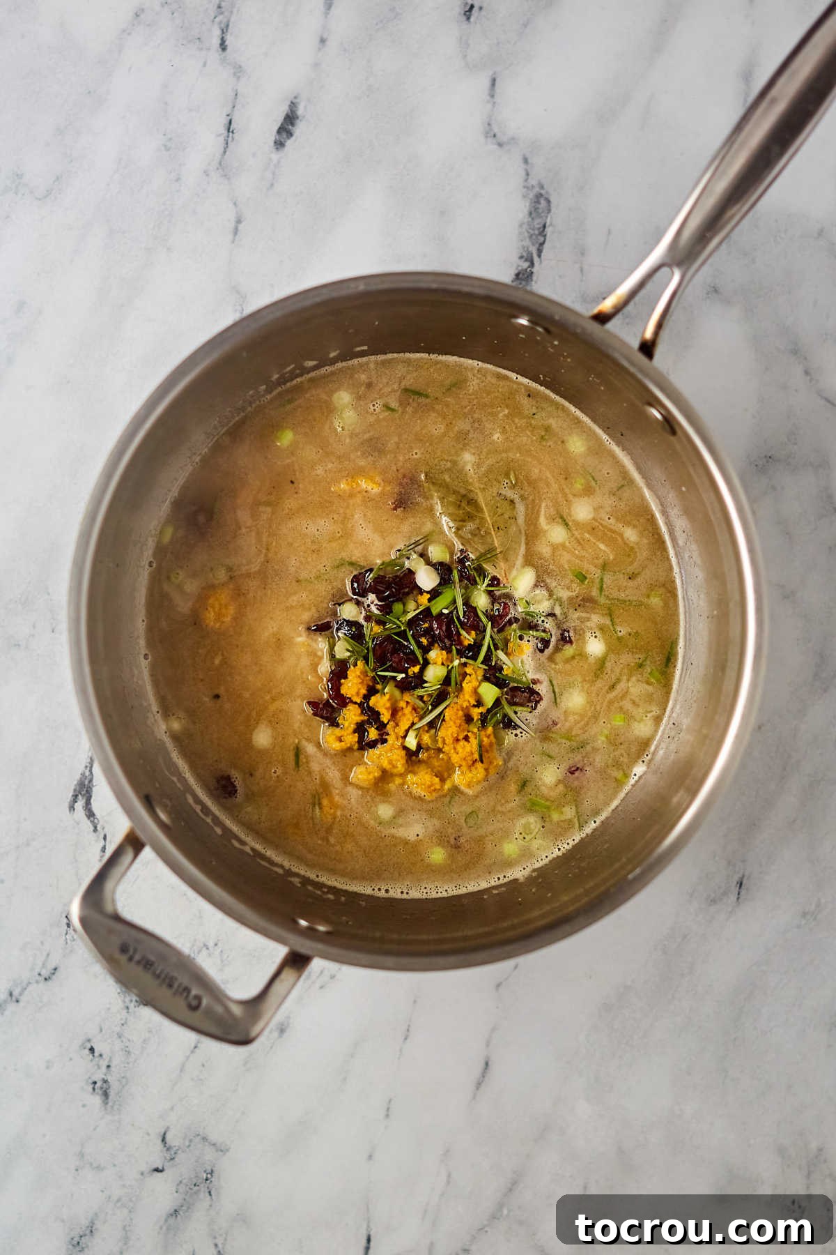 Pilaf Ingredients Ready to Cook A saucepan filled with white rice, chicken broth, dried cranberries, and orange zest, all mixed together and ready to be covered and simmered for the pilaf.