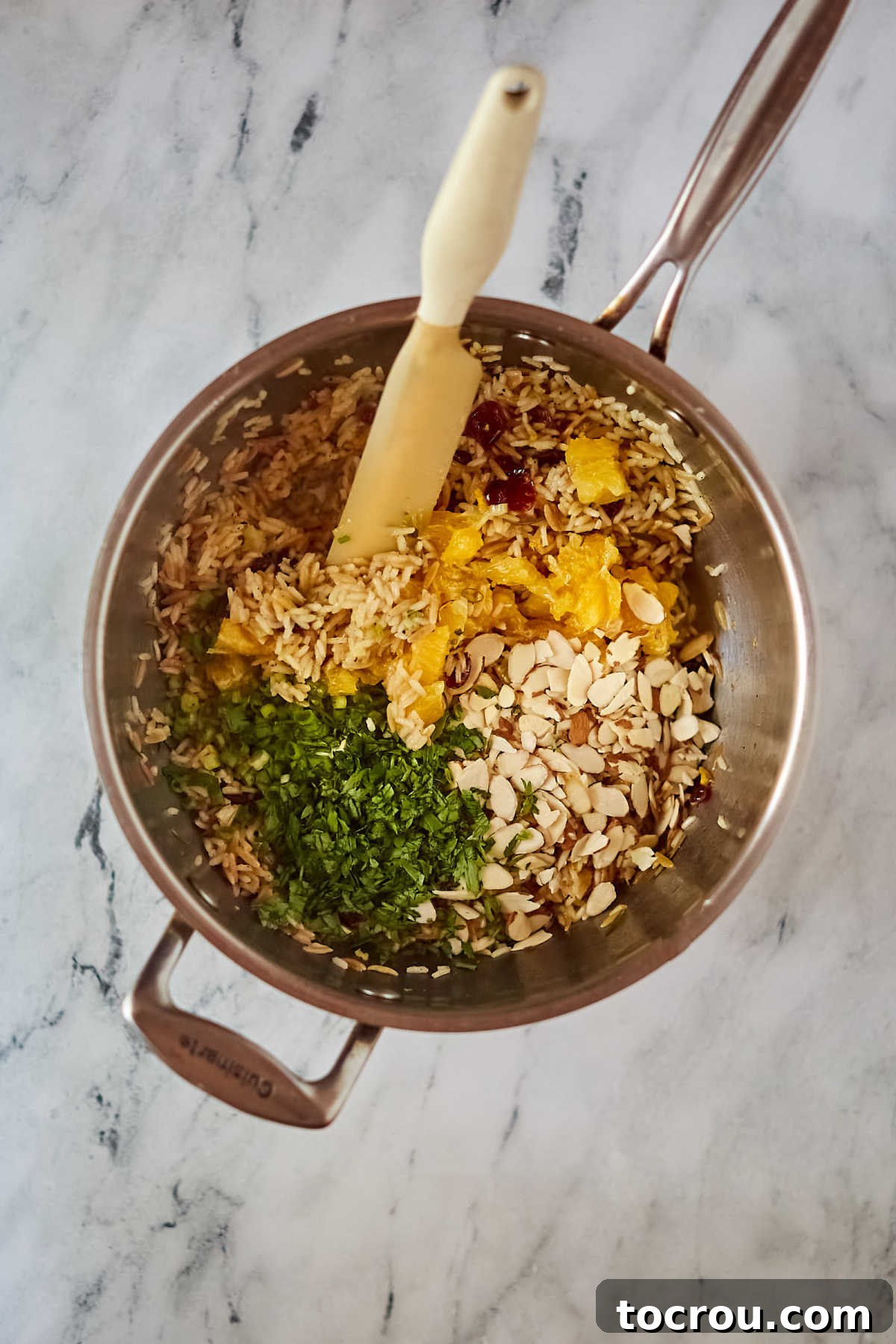 Stirring in Fresh Ingredients A hand stirring vibrant orange segments and freshly chopped parsley into a pot of cooked rice pilaf, showcasing the beautiful mix of colors and textures.