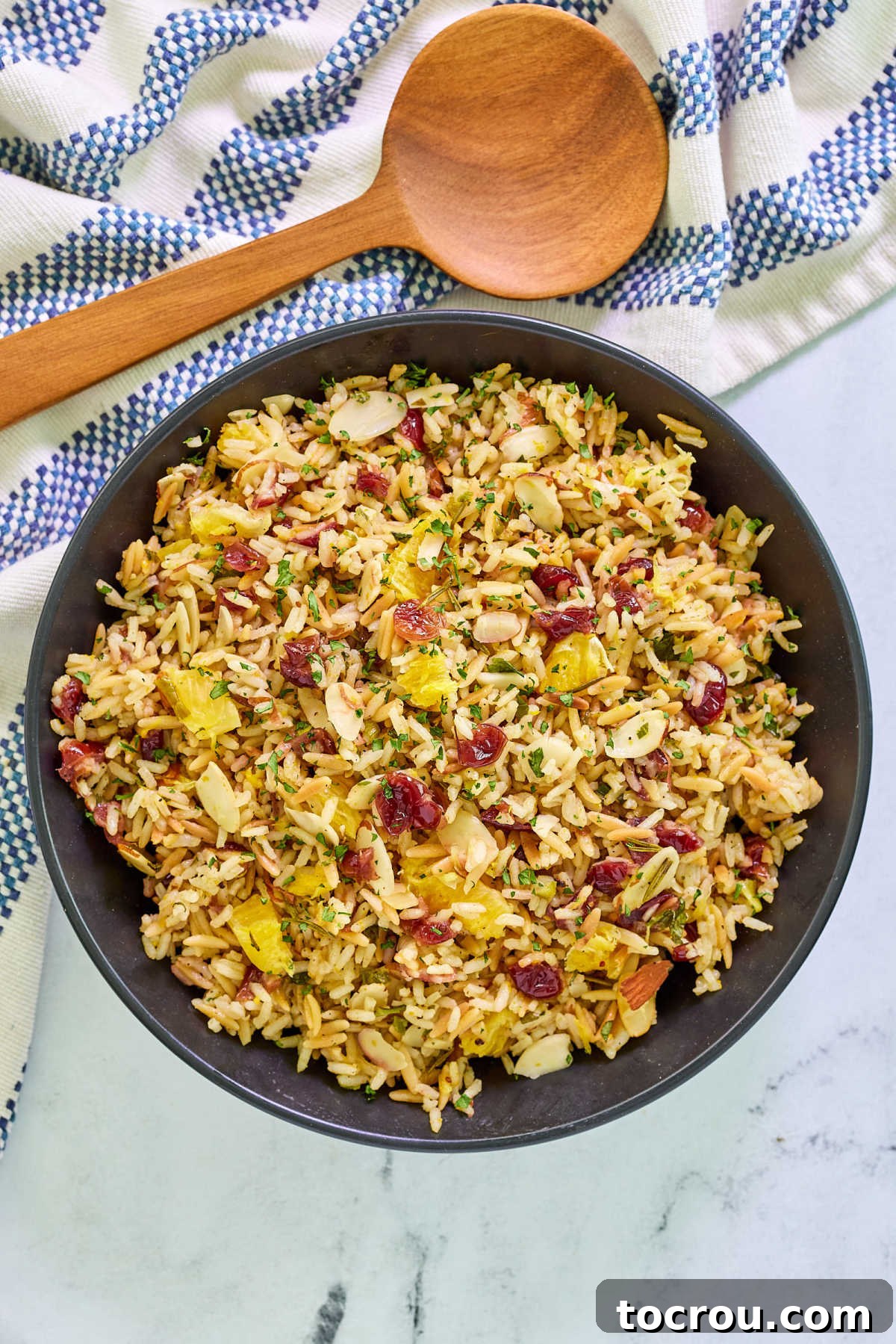 Serving Bowl of Rice Pilaf A beautifully presented serving bowl brimming with Cranberry Orange Rice Pilaf, generously garnished with fresh herbs, toasted slivered almonds, and vibrant cranberries. The fluffy texture of the rice and orzo is clearly visible.