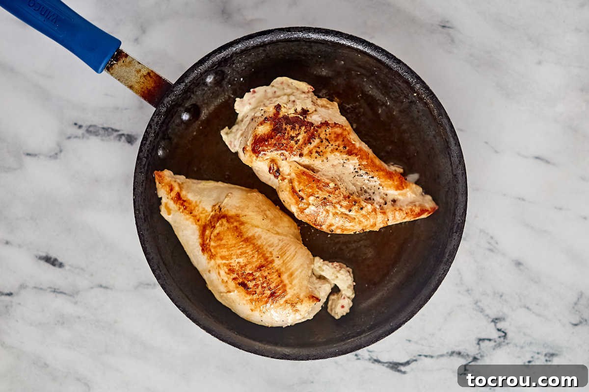 Creamy Jalapeno Popper Chicken 6 Stuffed chicken breasts in skillet showing deep golden color on the outside of the chicken after it has been browned.