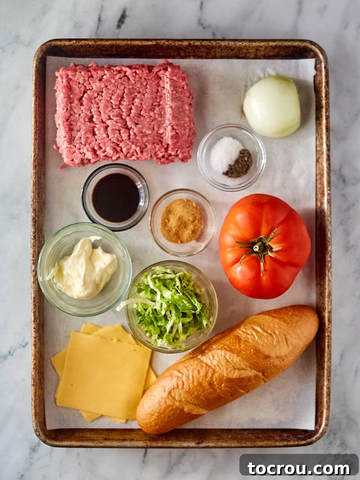 Ingredients including ground beef, onion, seasonings, american cheese, hoagie roll, mayonnaise, tomato, and lettuce ready to be made into a chopped cheese sandwich.