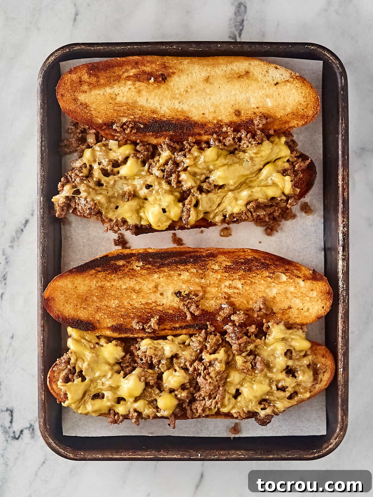 Toasted buns topped with ground beef mixture to make chopped cheese sandwiches, ready for toppings.