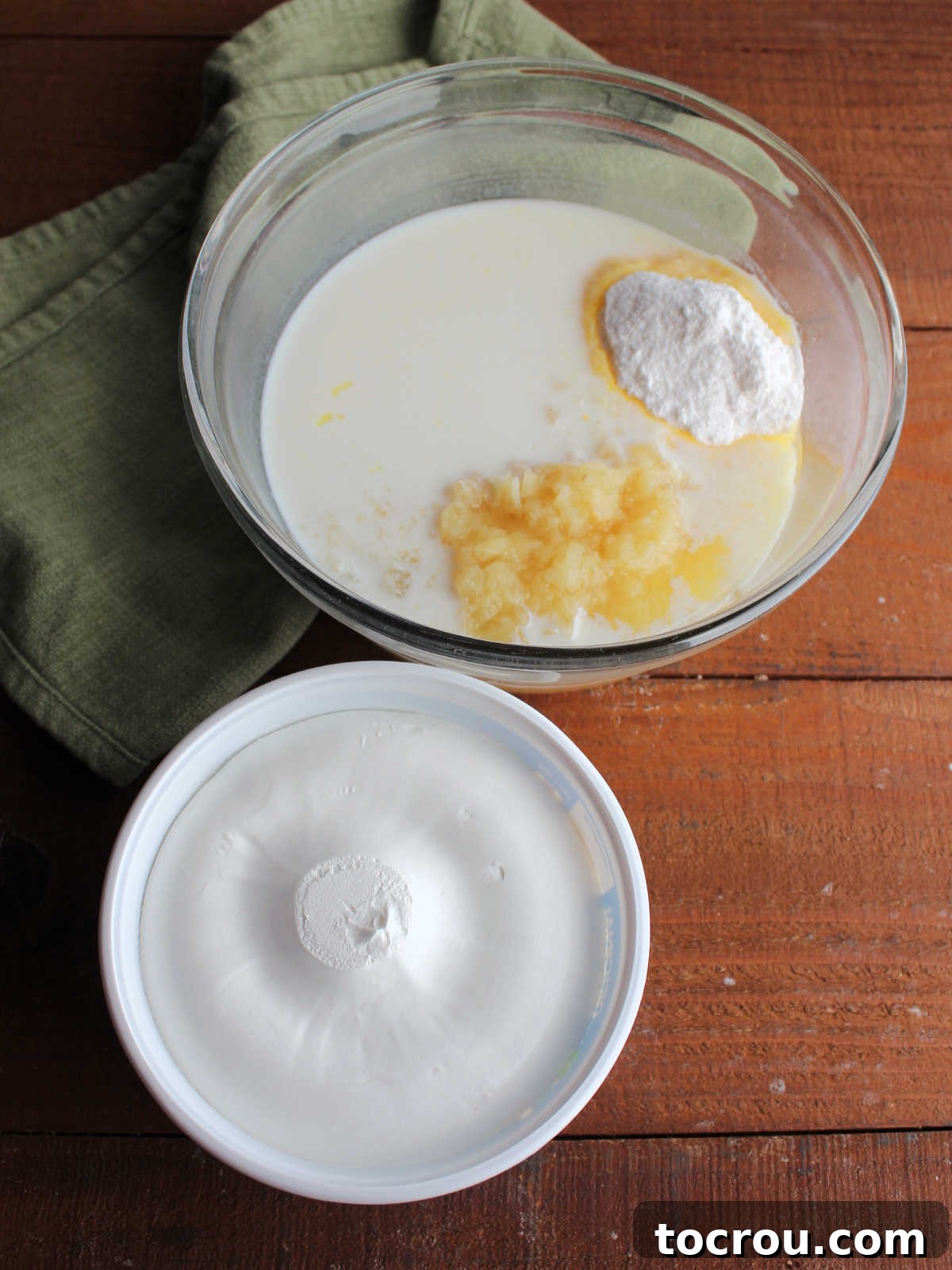 Frosting Ingredients A bowl filled with crushed pineapple, milk, and vanilla pudding mix, positioned next to a tub of Cool Whip, showcasing the components ready to be whipped into the cake's light and fluffy frosting.