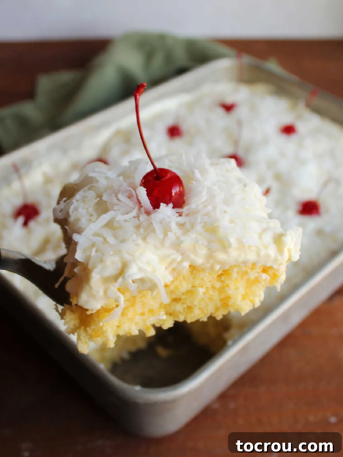 Texture of Ambrosia Poke Cake A spatula delicately lifting out a perfect slice of Ambrosia Poke Cake, revealing the moist orange cake texture, the fluffy pineapple topping, and the artful garnish of shredded coconut and a maraschino cherry.