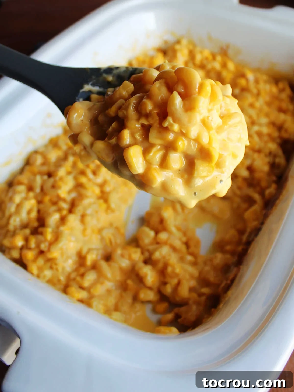 A serving spoon retrieving a portion of the cheesy macaroni and corn from the crockpot, highlighting the creamy texture.