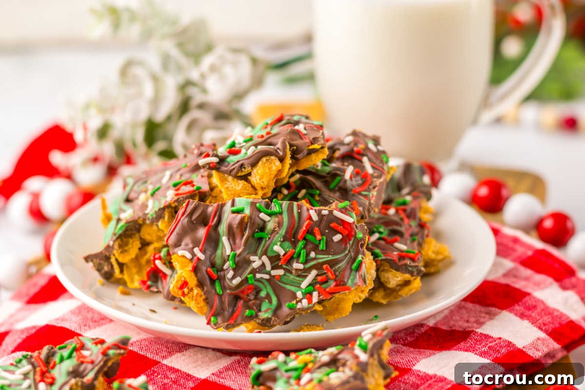 A plate piled high with pieces of golden cornflake brittle, featuring a crispy cereal layer beautifully topped with swirls of red and green candy melts over a rich chocolate layer. A glass of milk sits beside it, inviting enjoyment.