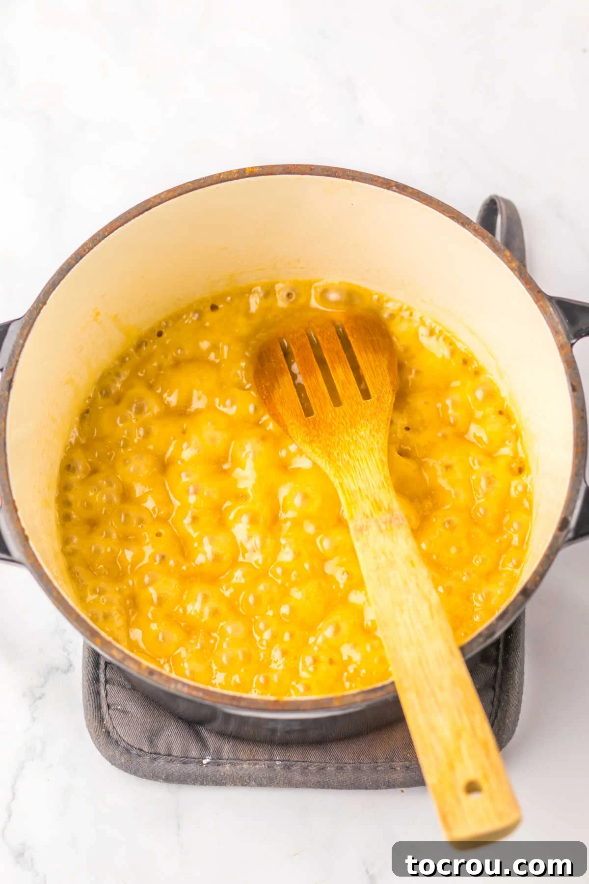 An enameled cast iron pan on a stovetop contains a bubbling mixture of melted butter and brown sugar, perfectly caramelizing.