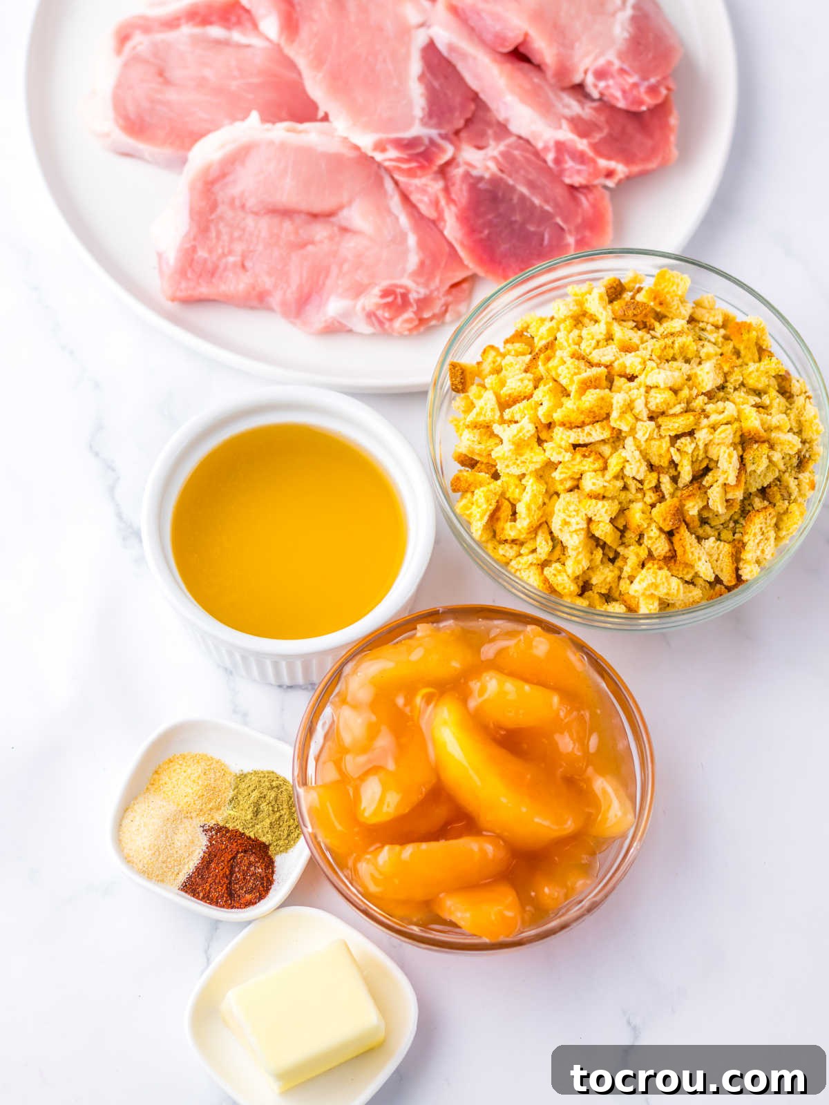 Ingredients including pork chops, cornbread stuffing mix, apple pie filling, butter, seasonings, and chicken broth ready to go in the slow cooker. 