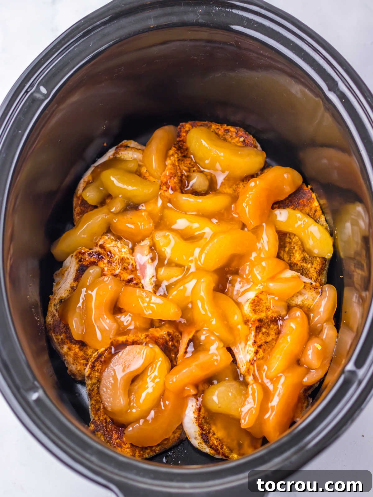 Apple pie filling distributed over the pork chops in a crockpot. 