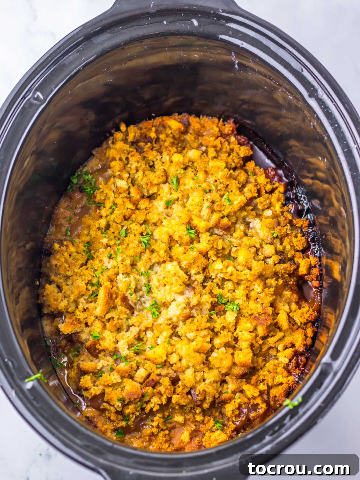 Cooked crockpot pot pork chops and apples with stuffing on top and golden brown edges around the crockpot, ready to serve. 