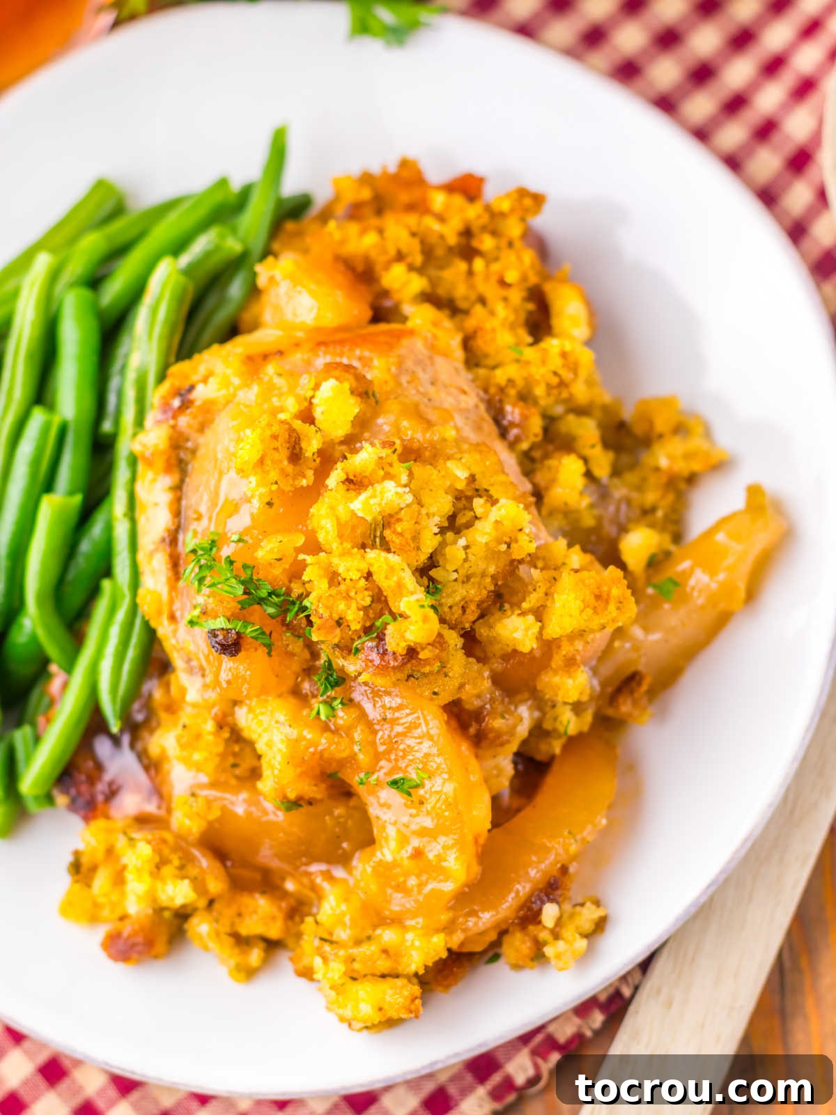 Close up of cooked pork chops with apple pie filling and cornbread stuffing on dinner plate with green beans. 
