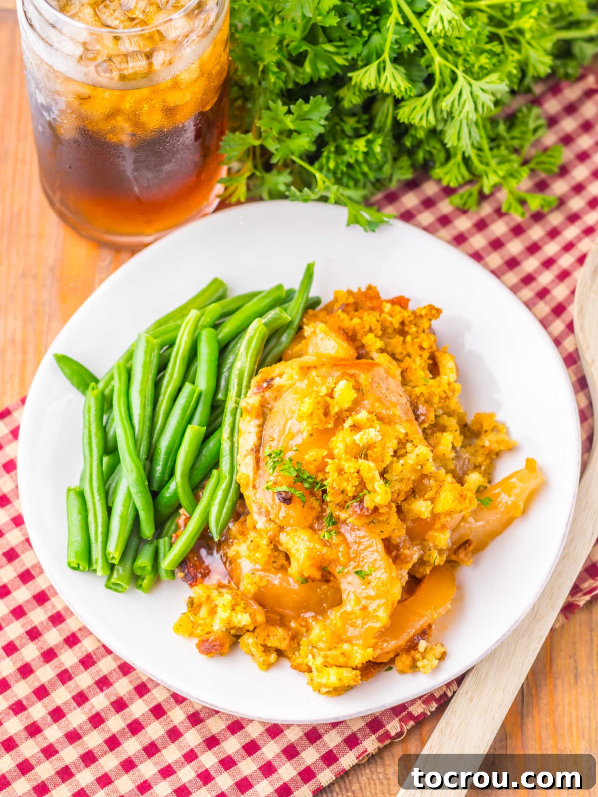 Dinner plate with slow cooked pork chops with apples and stuffing served with green beans and iced tea. 