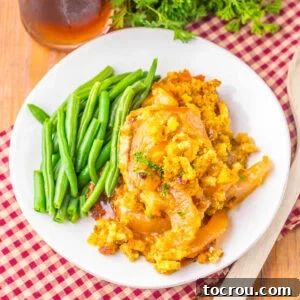 Plate with pork chops cooked with apple pie filling and cornbread stuffing in a crockpot served with green beans.