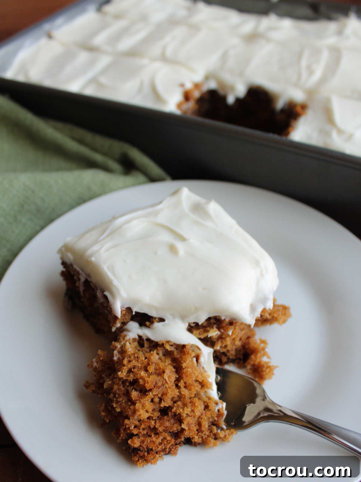 A fork poised to take a bite of moist applesauce spice cake, adorned with creamy cream cheese frosting, highlighting its tempting texture.