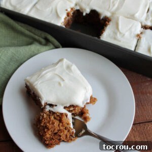 A fork taking a piece of applesauce cake, revealing its rich brown color from cinnamon, cloves, and allspice, with plump raisins embedded, and topped with a generous swirl of cream cheese frosting.