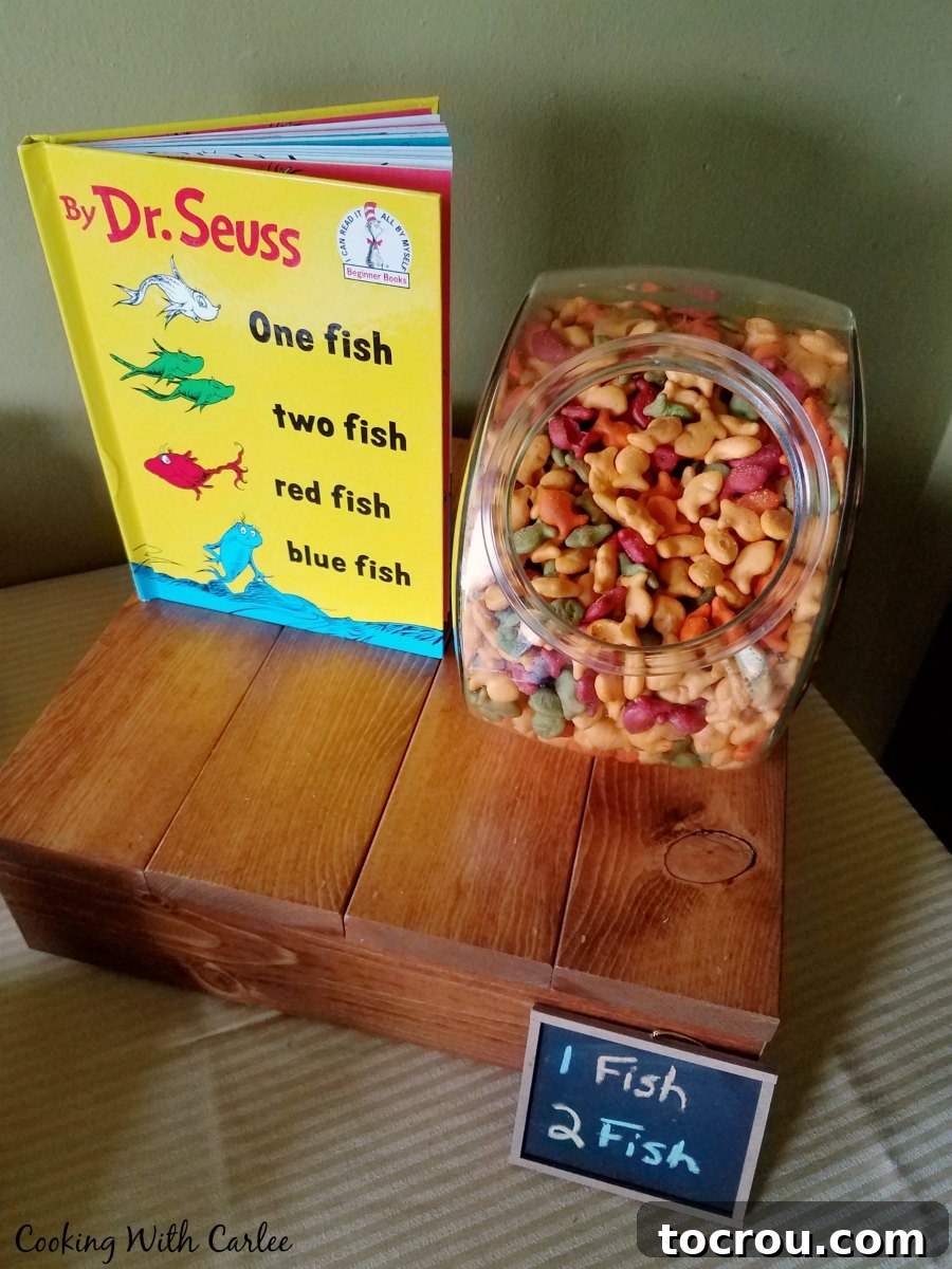 One Fish, Two Fish Snacks Cookie jar filled with goldfish crackers next to a 'One Fish Two Fish Red Fish Blue Fish' book, perfectly themed for a Dr. Seuss party.