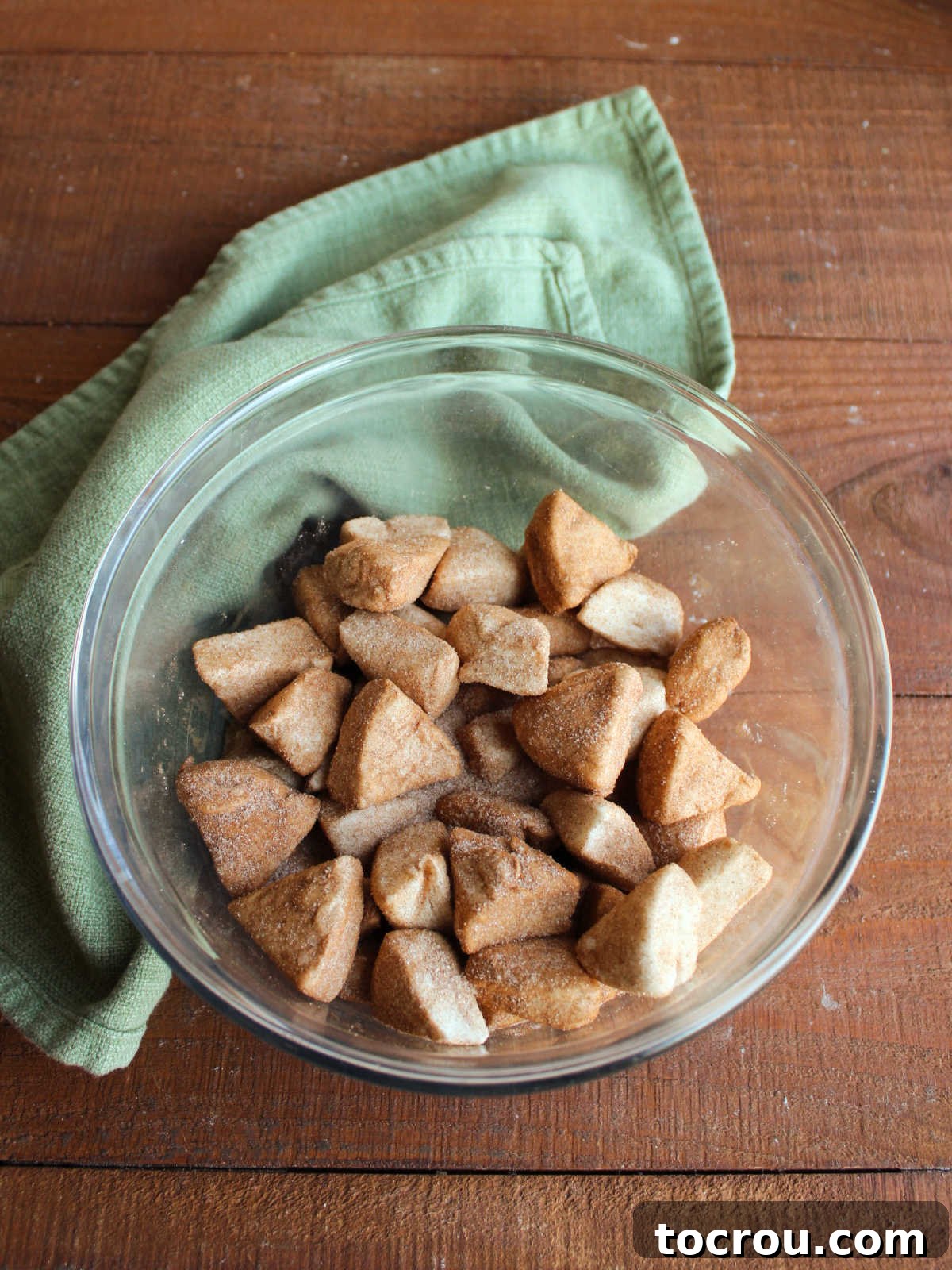 Mixing bowl filled with pieces of biscuit dough tossed in cinnamon sugar mixture.