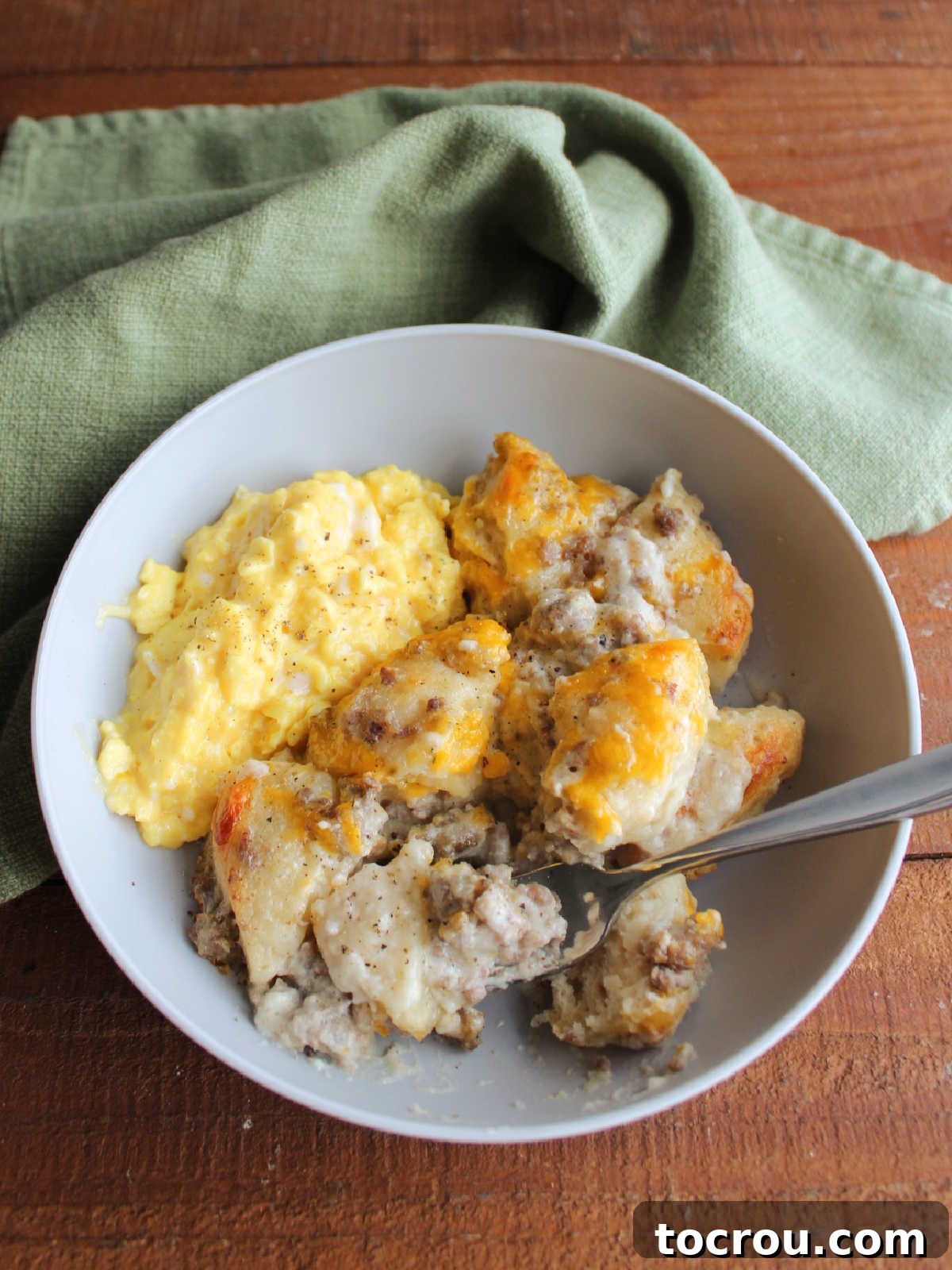 Biscuits and Gravy with Scrambled Eggs A bowl of savory sausage and gravy bubble up bake served hot with soft, creamy scrambled eggs on the side, creating a complete and satisfying breakfast meal.