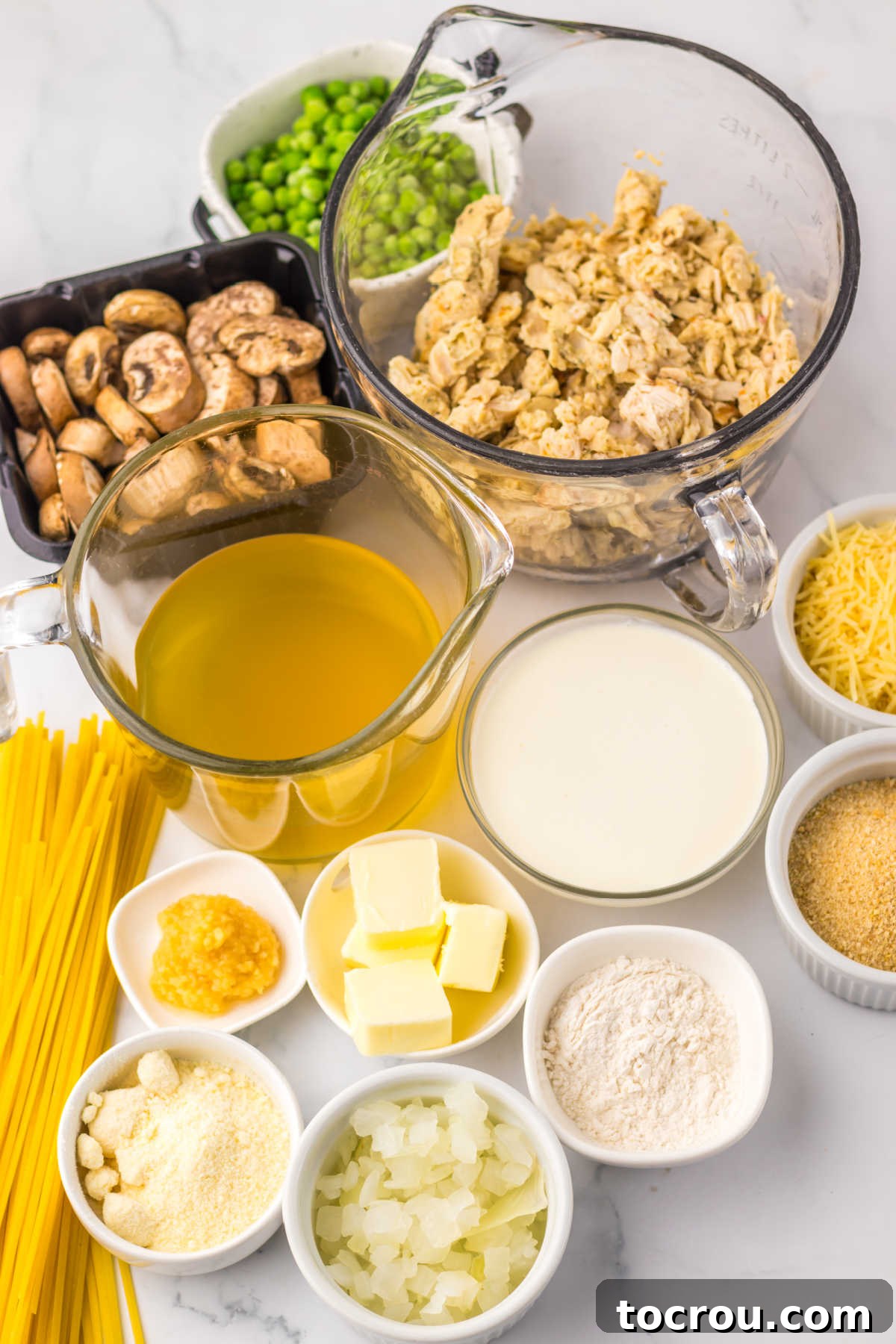 Ingredients including leftover turkey, mushrooms, peas, butter, parmesan cheese, cream, garlic, onion and pasta, ready to be made into turkey tetrazzini.