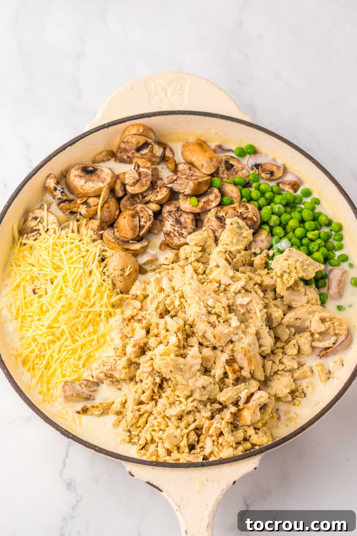 Large skillet with creamy sauce topped with chunks of turkey, peas, mushrooms, and cheese ready to be stirred in.