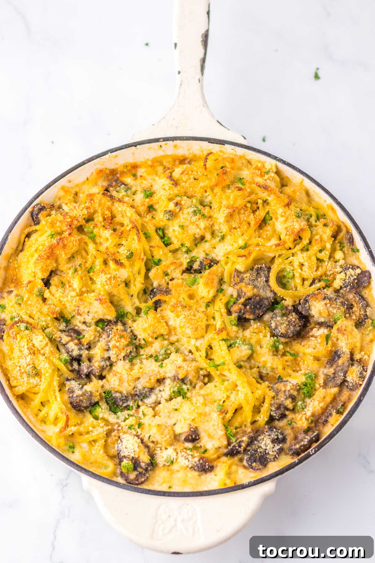 Skillet of baked turkey tettrazini with melted cheese and browned bread crumbs on top, ready to be served.