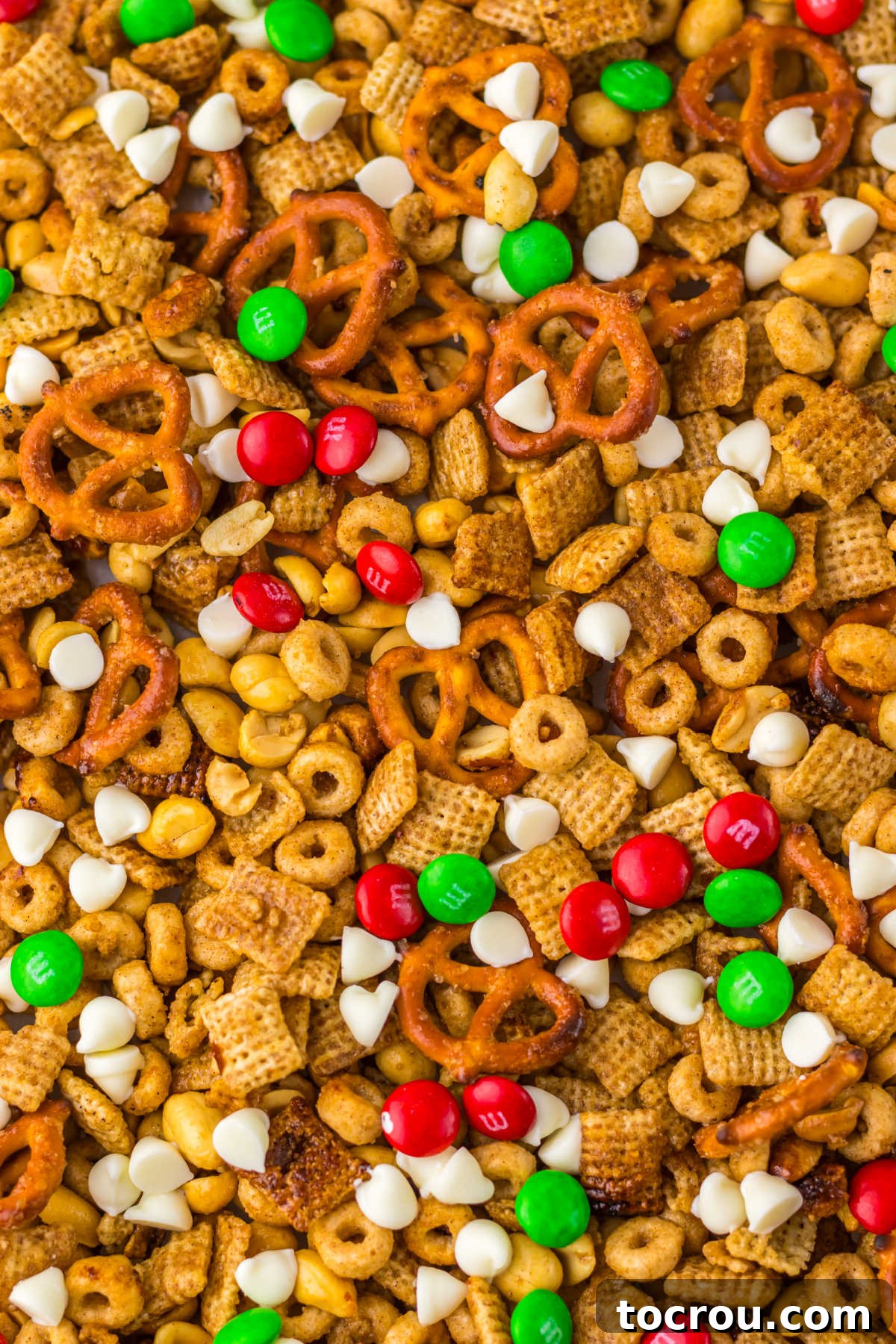A close-up of maple cinnamon Chex mix, generously sprinkled with festive holiday candies and smooth white chocolate chips, creating a visually appealing and delicious sweet snack.