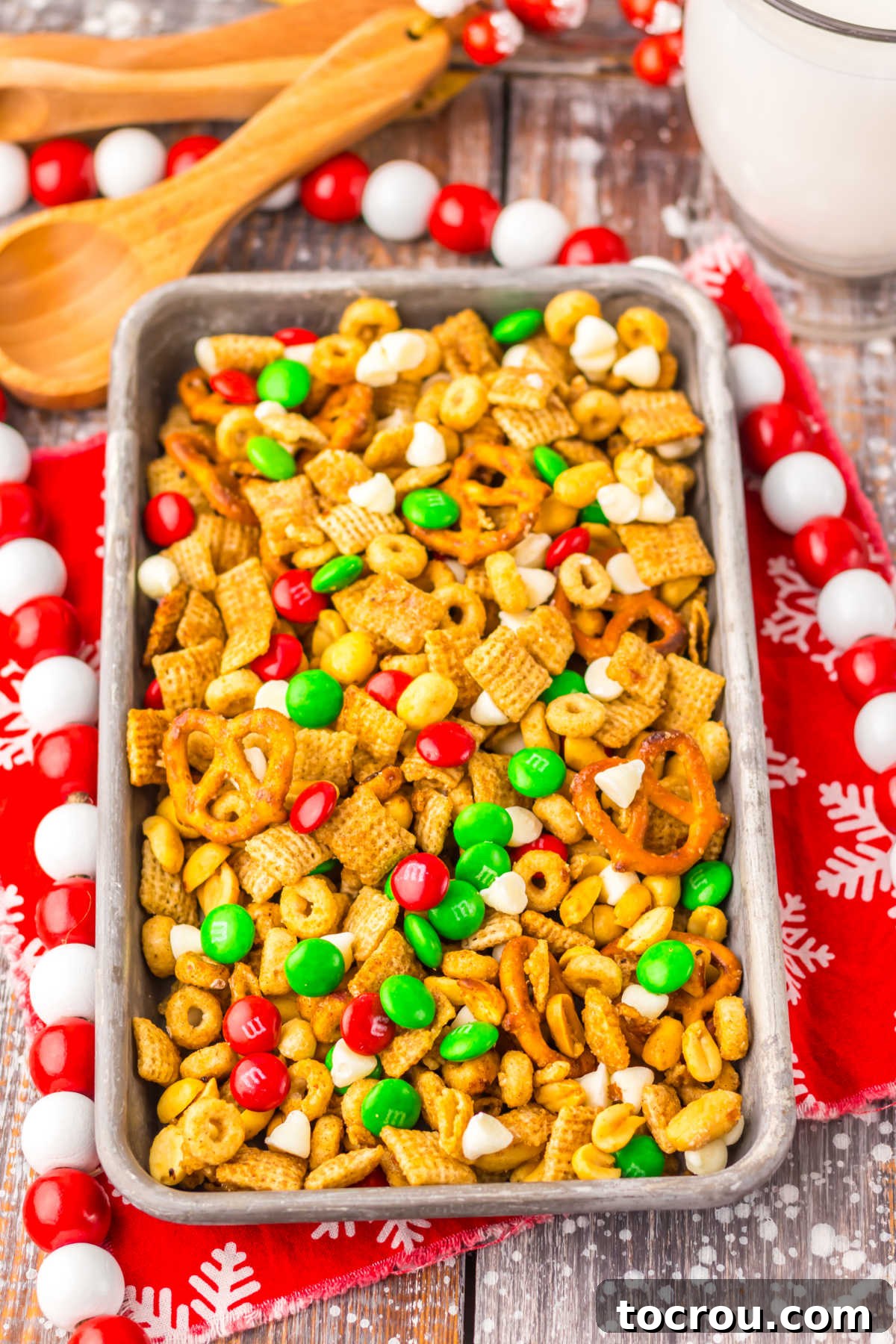 A large tray showcasing a batch of Christmas Chex mix, featuring a rich cinnamon brown sugar coating, perfectly mixed with colorful holiday M&Ms and creamy white chocolate chips.