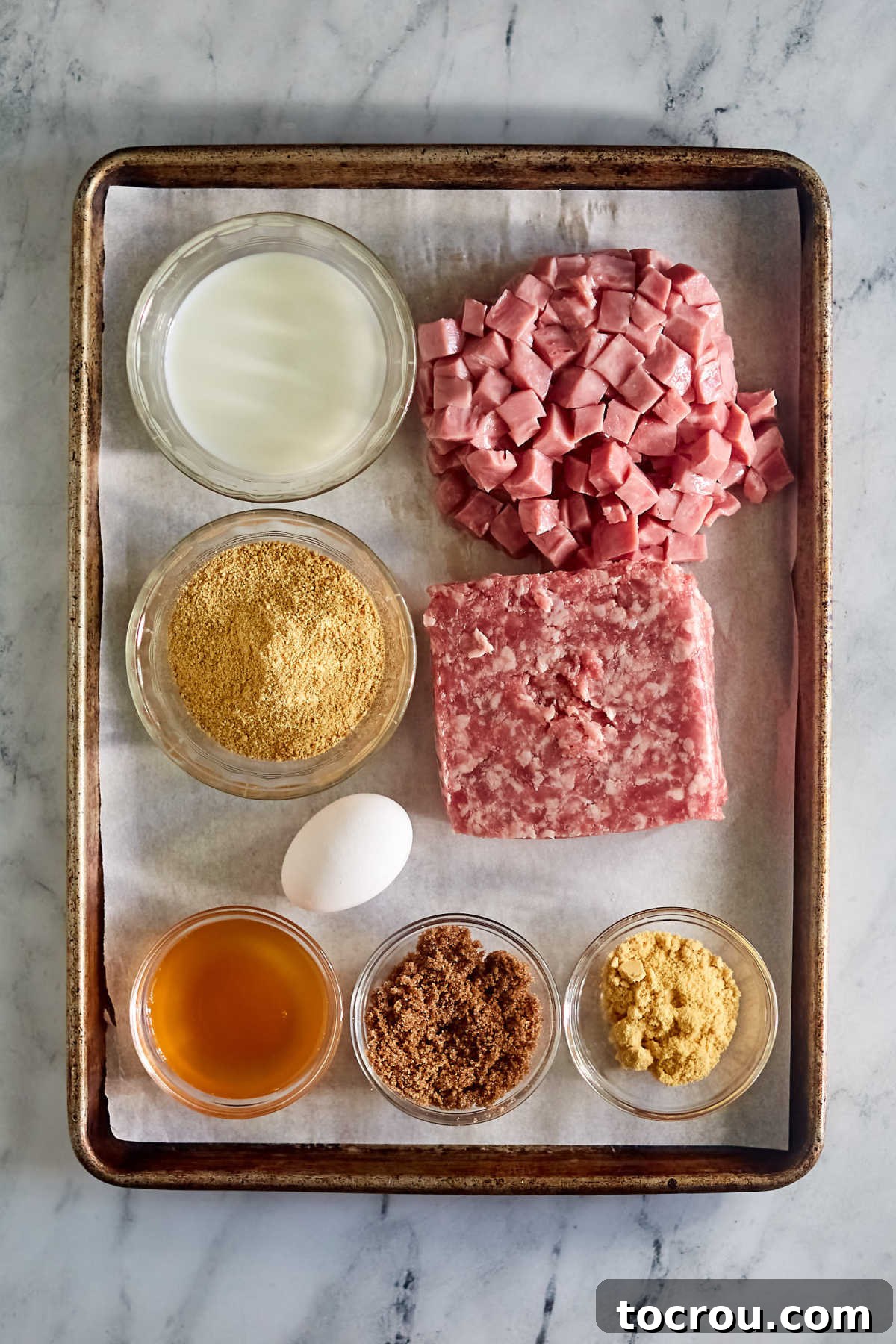 A vibrant flat lay of all the fresh ingredients required to make a delicious glazed ham loaf, including chunks of ham, ground pork, graham cracker crumbs, milk, egg, brown sugar, mustard powder, and vinegar, meticulously arranged and ready for preparation.