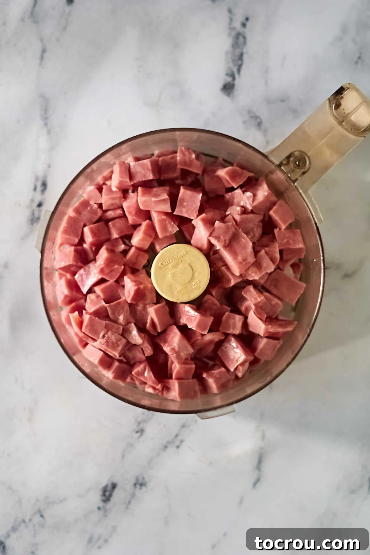 Close-up shot of raw ham chunks nestled in a food processor, poised for grinding to create the perfect texture for a homemade ham loaf.