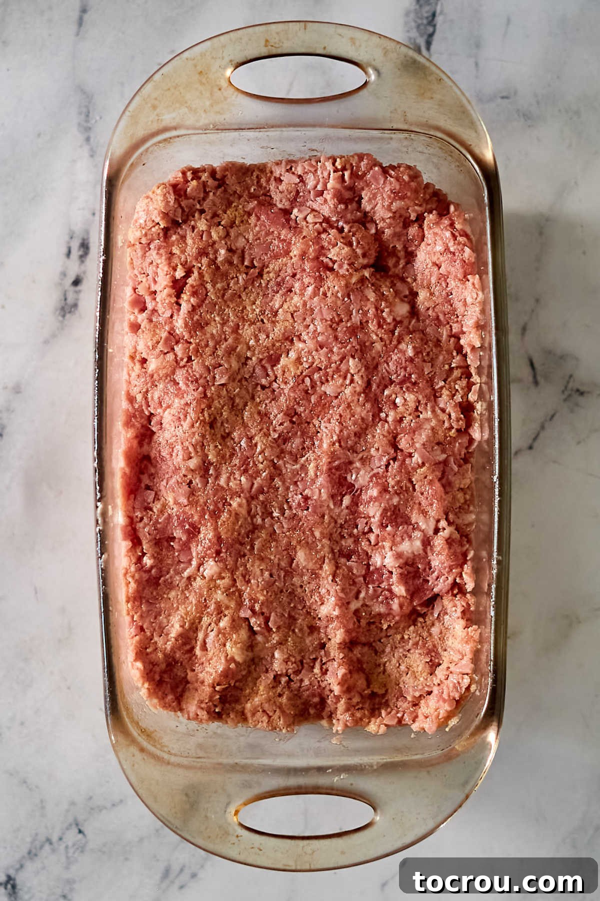 A perfectly shaped ham loaf mixture nestled in a glass loaf pan, ready for the application of its signature glaze before baking to golden perfection.