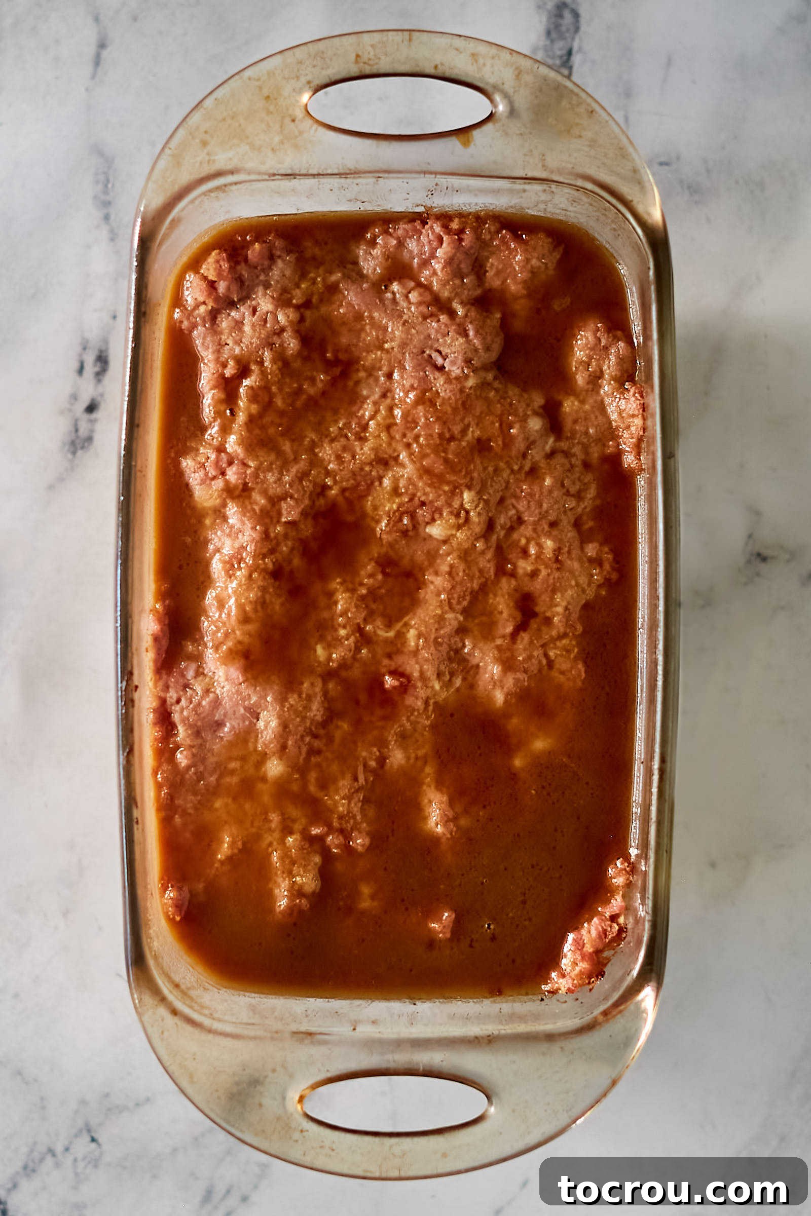 A freshly prepared glazed ham loaf glistening in a glass loaf pan, perfectly ready to be placed into the oven for baking.