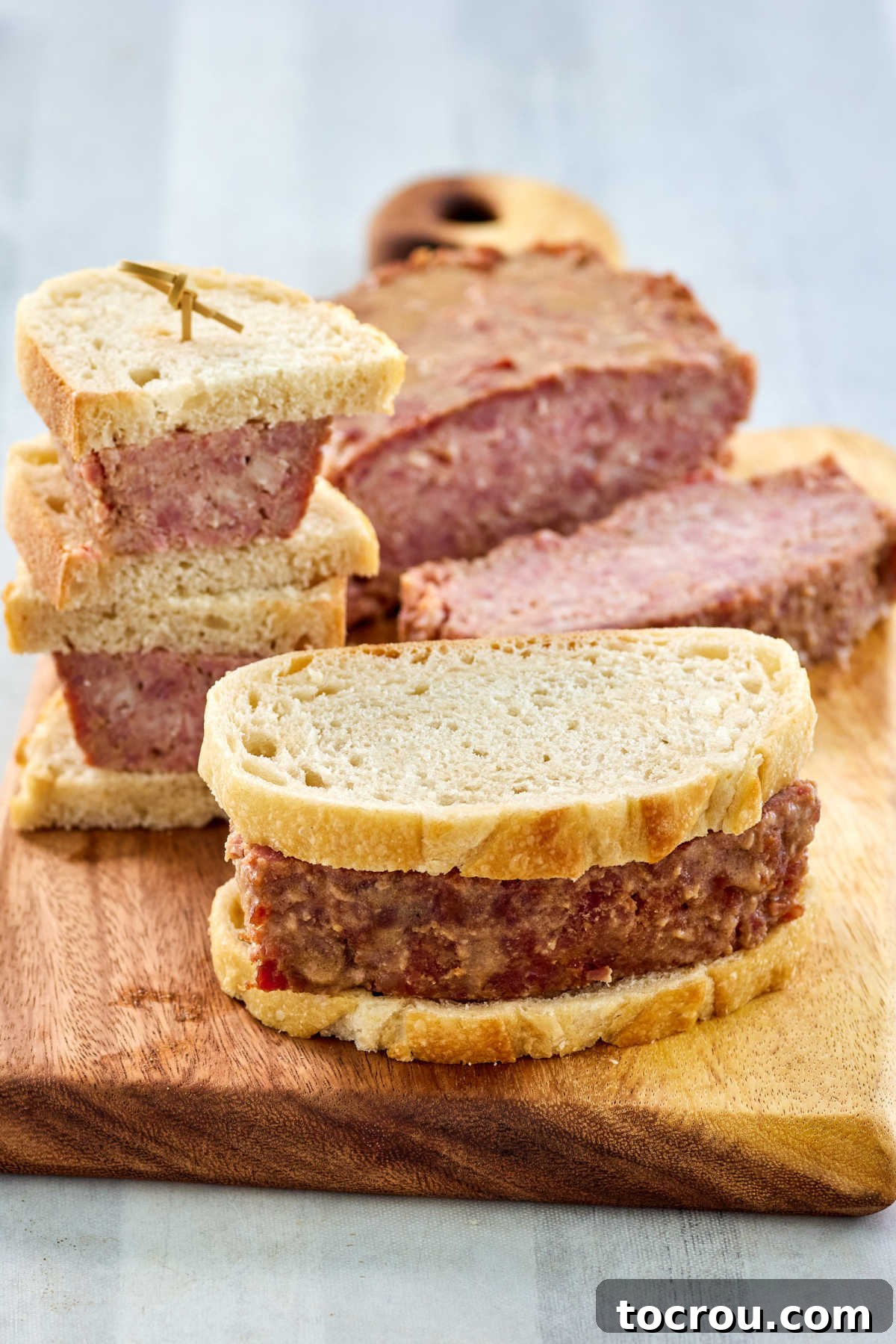 Thick, juicy slices of glazed ham loaf artfully arranged, with a couple of slices transformed into a hearty sandwich on robust bread, ready to be enjoyed.