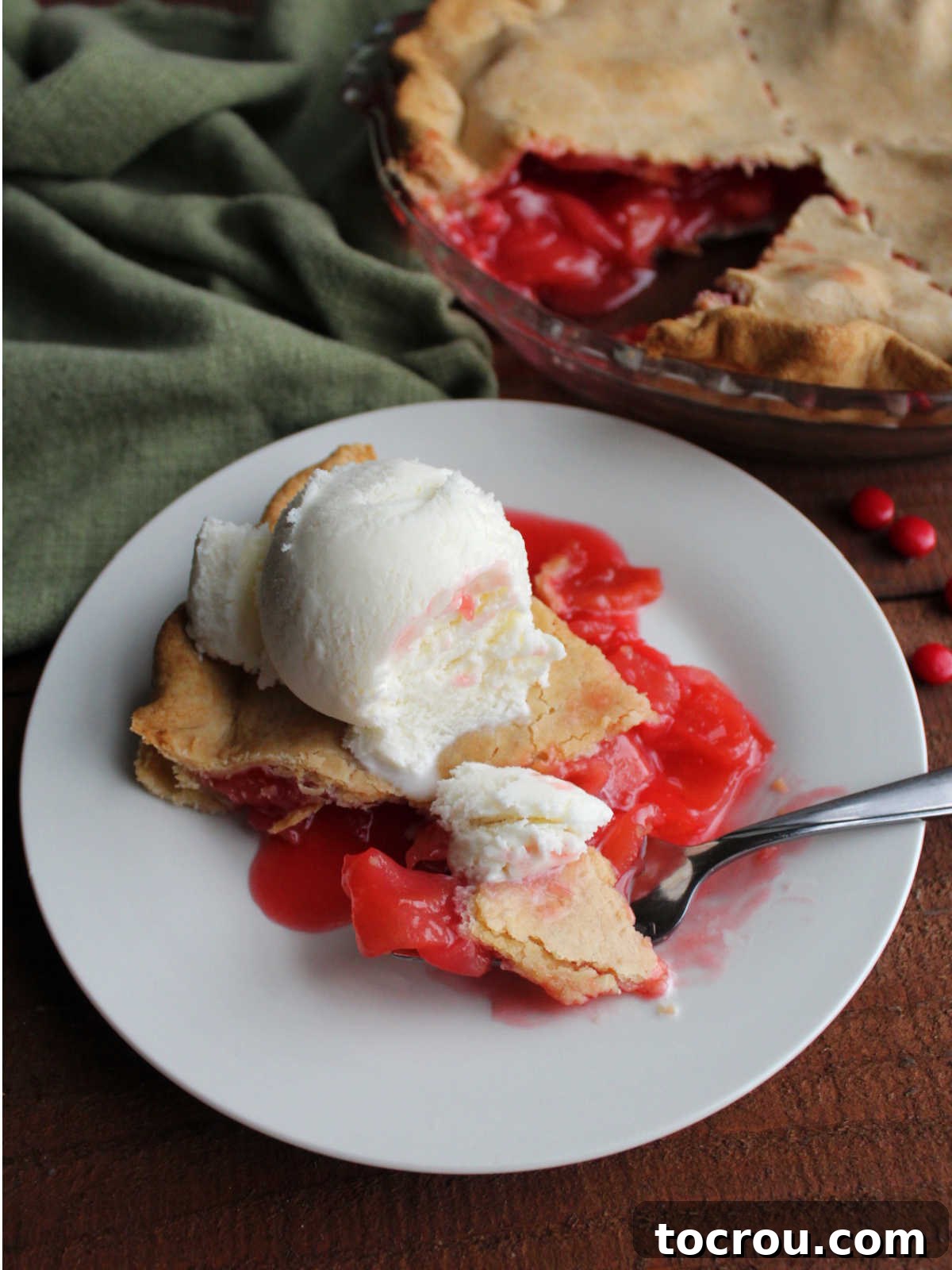 Bite of red hot apple pie with some vanilla ice cream on fork next to the rest of the slice of pie, ready to eat.