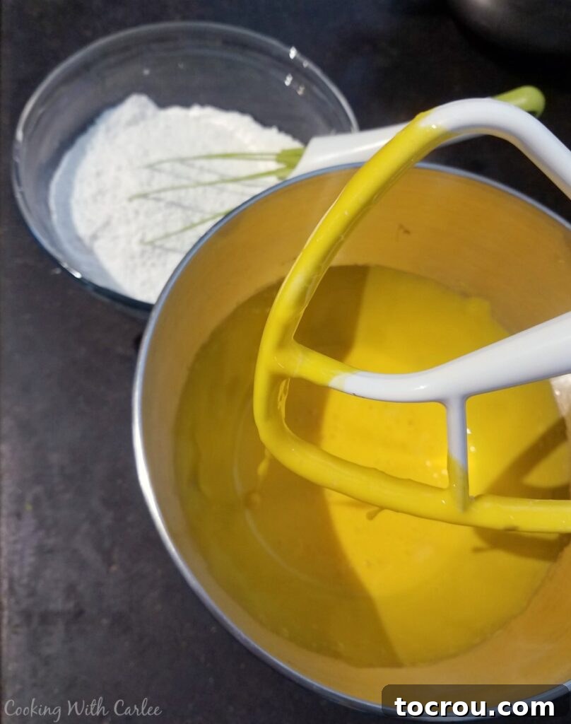 Whipped Egg Yolks for Gold Cake Whipped egg yolks in a mixer bowl, with a bowl of flour in the background, showcasing the initial steps of the gold cake preparation.
