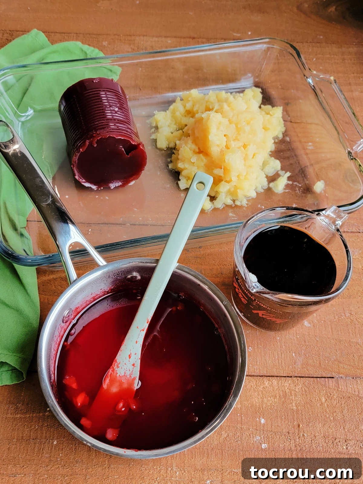 Ingredients for Frosted Cranberry Jello Salad, including canned crushed pineapple, a box of cherry Jell-O, jellied cranberry sauce, and a bottle of Coca-Cola, laid out on a kitchen counter.