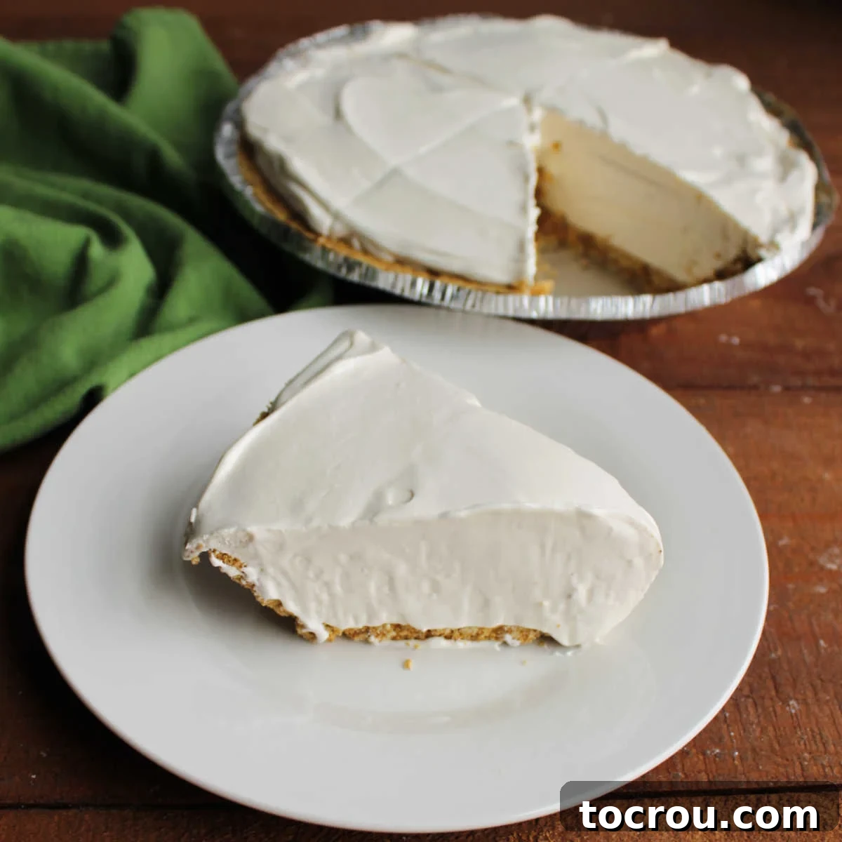 Frozen Key Lime Pie Slice Slice of creamy frozen key lime pie with fluffy filling in graham cracker crust on plate with remaining pie in background. The texture is soft, not icy.
