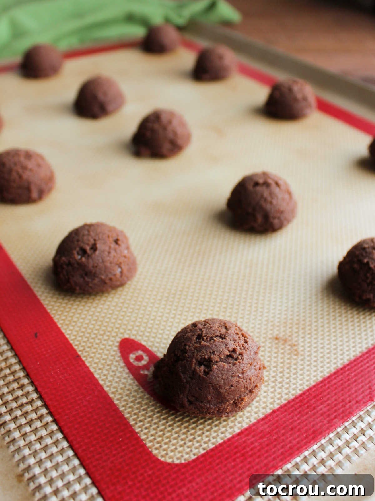 Oreo Dream Blossoms 5 Small, uniformly scooped portions of chocolate cookie dough are neatly arranged on a silicone mat-lined cookie sheet, spaced perfectly and ready to enter the oven for baking.