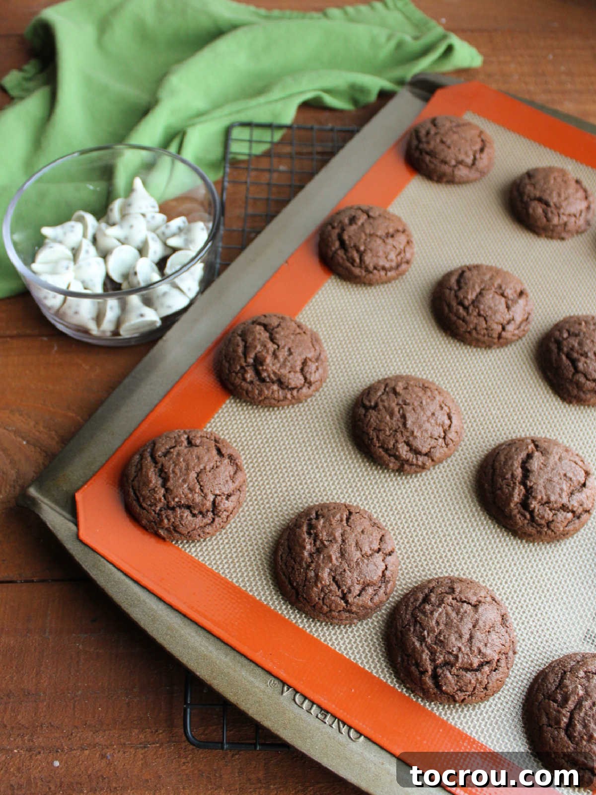 Oreo Dream Blossoms 6 Puffy, freshly baked chocolate cookies cool gently on a baking sheet, their inviting aroma filling the air. Alongside, a bowl overflows with unwrapped Hershey's Kiss candies, poised to be pressed into the warm cookies.