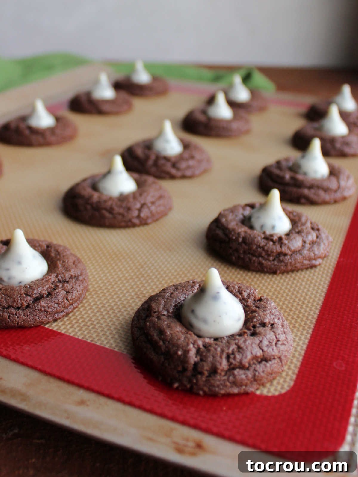 Oreo Dream Blossoms 7 A close-up shot of warm chocolate cookies still on the baking sheet, each one perfectly cradling a white chocolate Cookies and Cream Hershey's Kiss nestled in its soft center.
