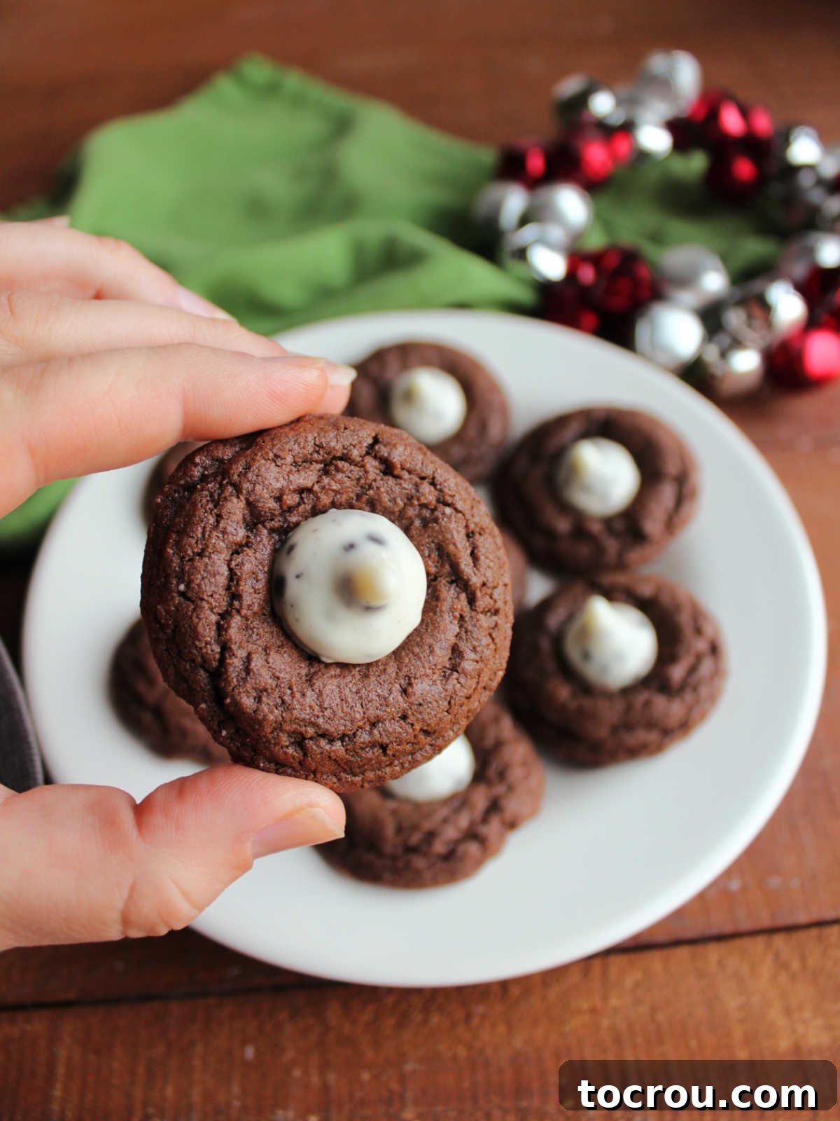 Oreo Dream Blossoms 10 A hand gently holds a single Cookies and Cream Blossom cookie, perfectly showcasing its soft chocolate base and creamy white chocolate Kiss, ready for an indulgent bite.