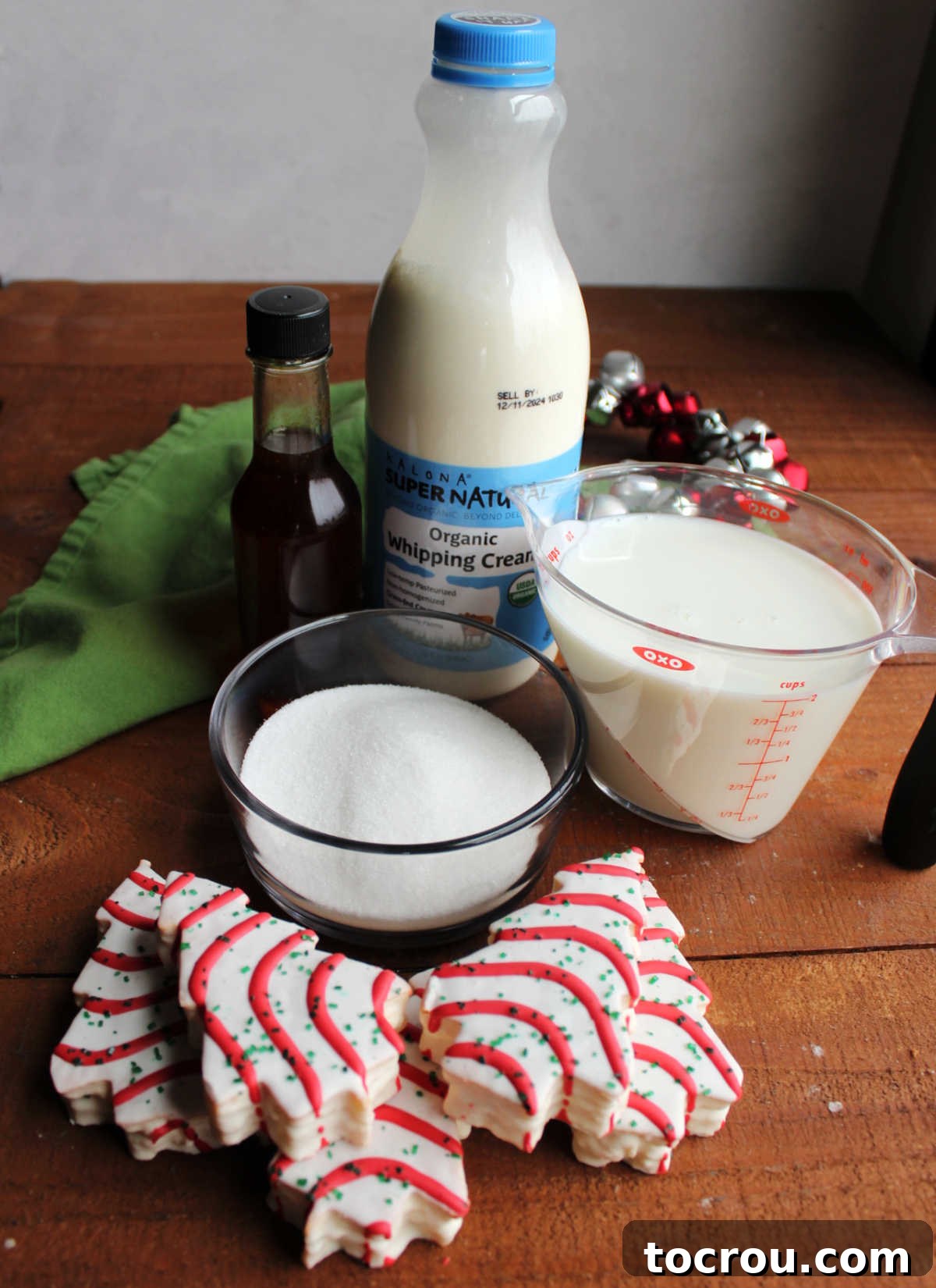 A collection of ingredients for homemade Christmas tree cake ice cream including several Little Debbie Christmas tree cakes, granulated sugar, whole milk, heavy cream, and a bottle of vanilla extract, neatly arranged on a countertop, ready for the ice cream making process.