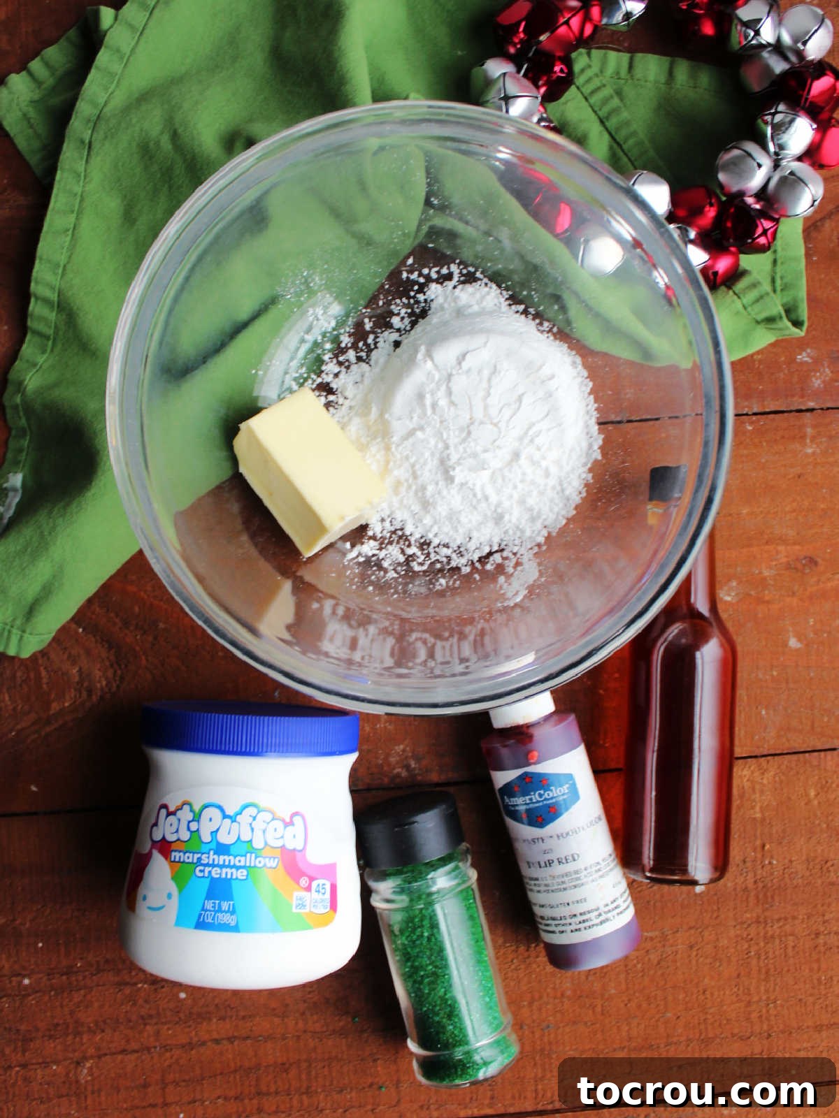 Key ingredients for homemade marshmallow fluff buttercream frosting displayed on a surface, featuring a block of softened butter, powdered sugar, a bottle of vanilla extract, and a container of marshmallow fluff, prepared for mixing.