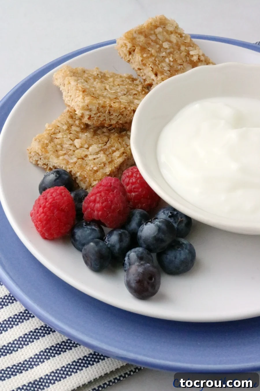 A beautifully arranged breakfast featuring fresh berries, a bowl of creamy yogurt, and three perfectly cut brown sugar oatmeal bars.
