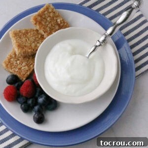 Bowl of vanilla yogurt next to three squares of brown sugar oat bars and fresh berries.