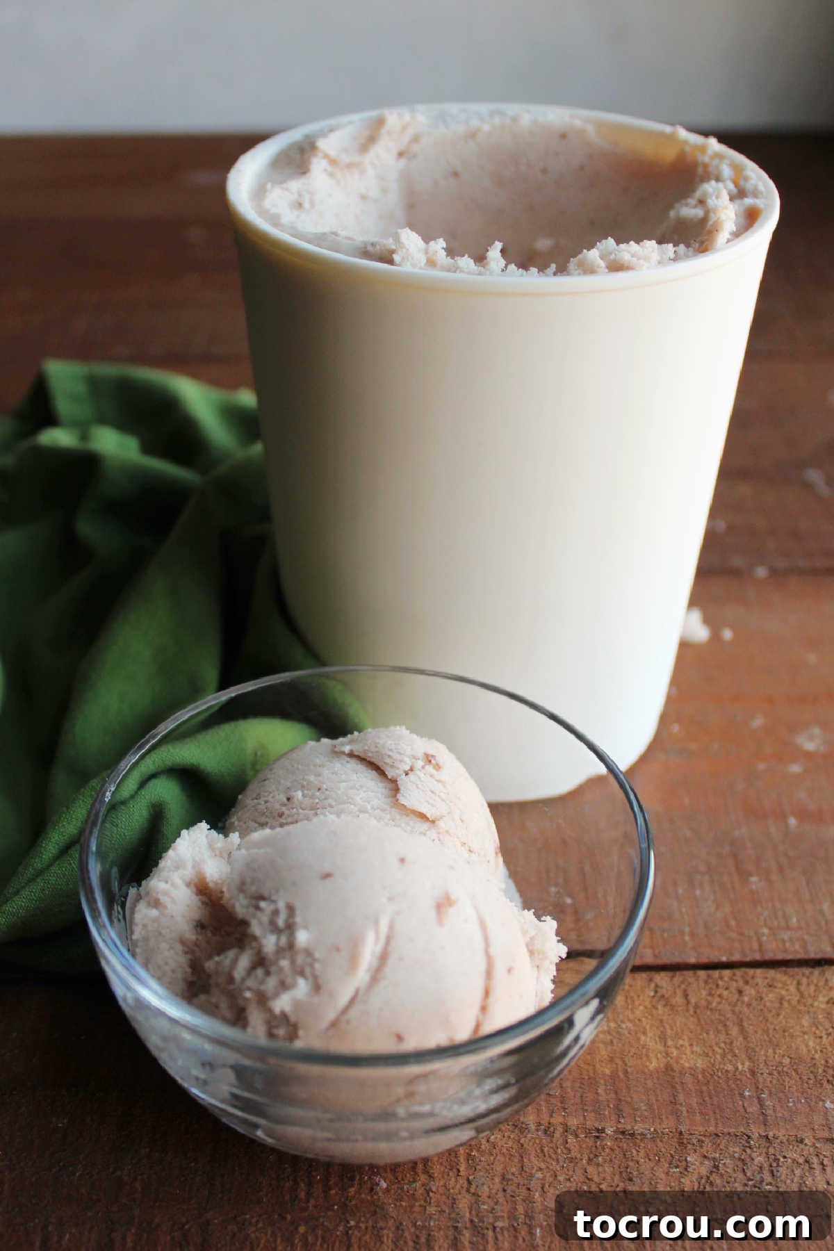 Scoops of apple butter ice cream in a small glass bowl in front of a storage container of more homemade ice cream.