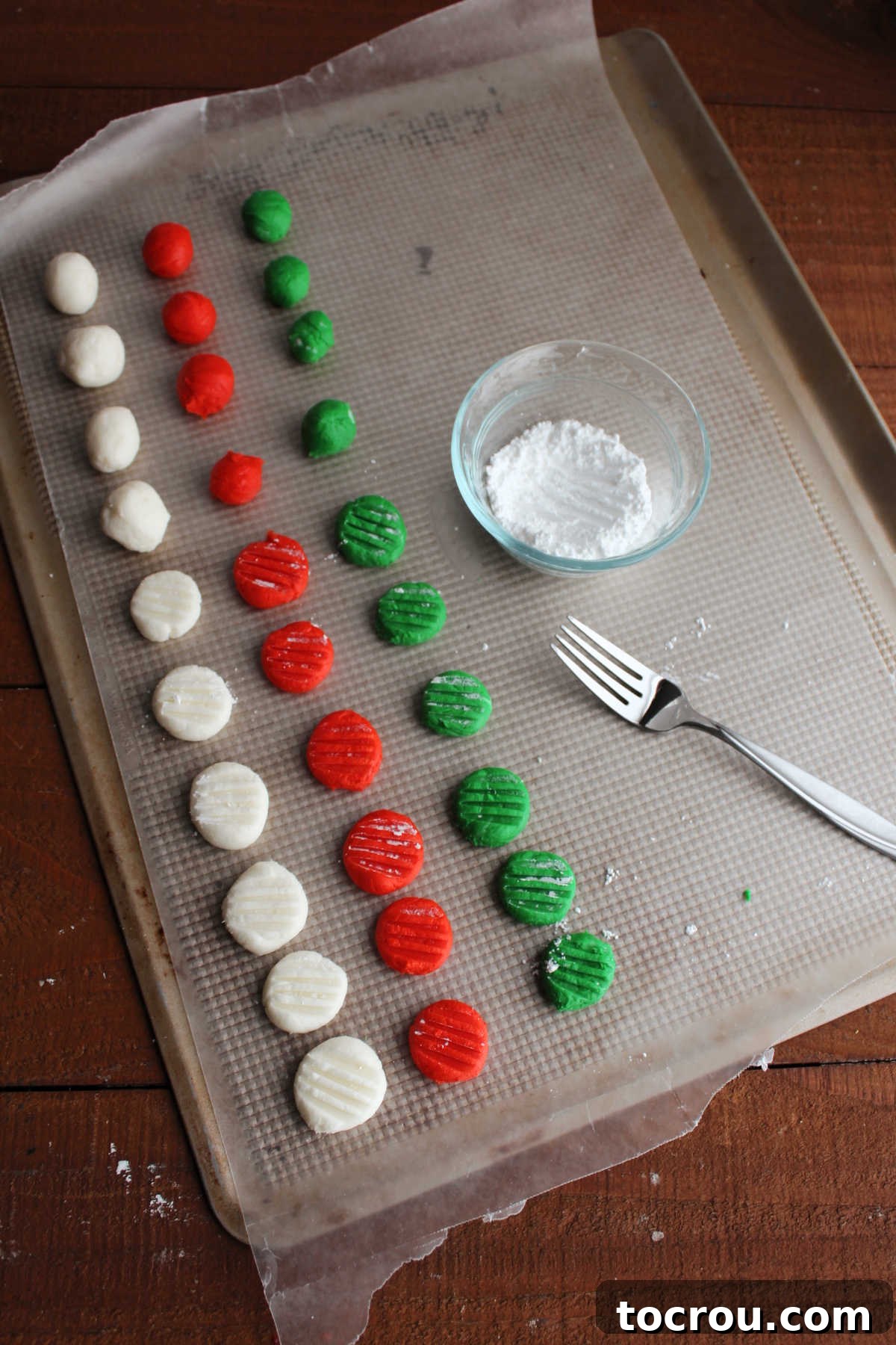Creamy Dream Mints 5 Round cream cheese mints being pressed down with a fork that has been dipped in powdered sugar.
