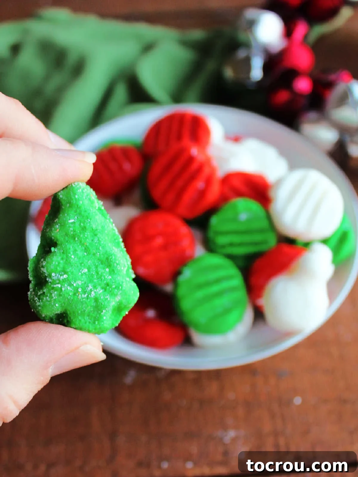 Creamy Dream Mints 7 Hand holding a green cream cheese mint in the shape of a Christmas tree with more mints in the background.