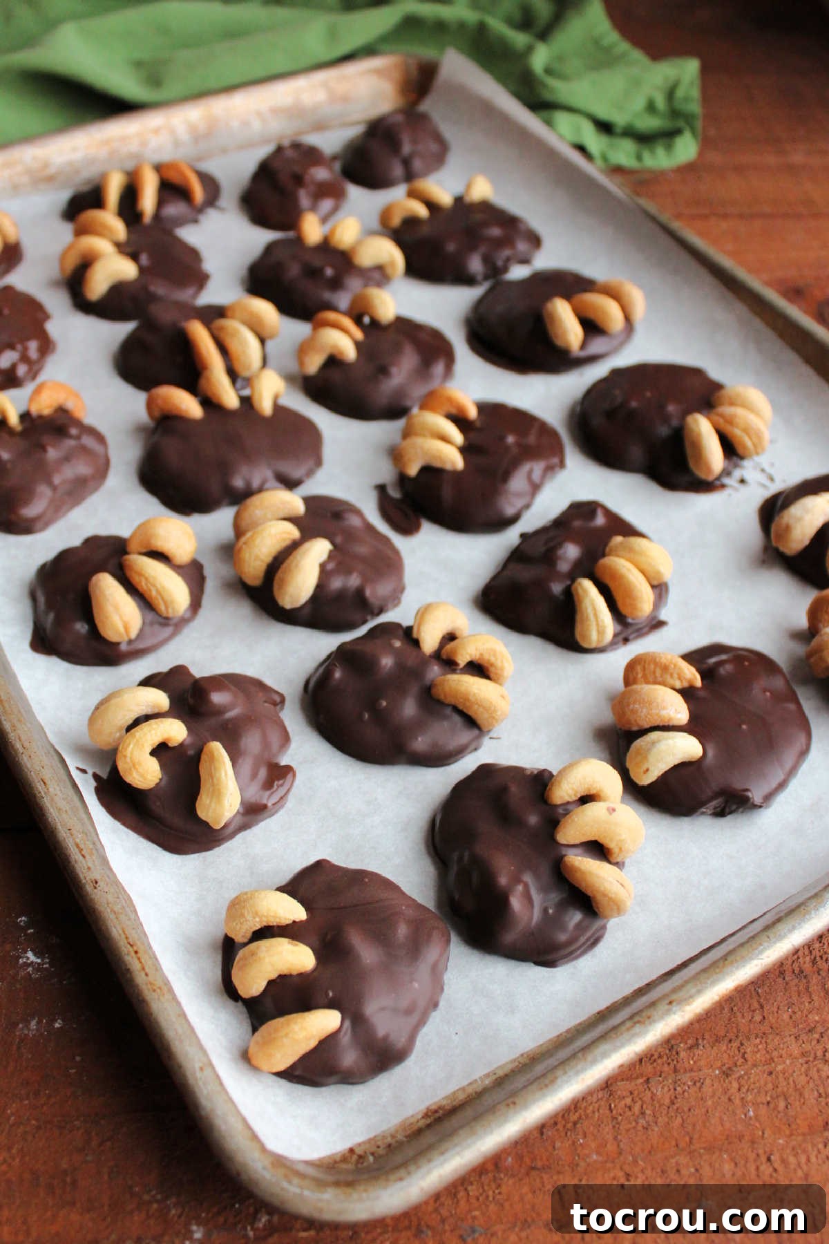 A baking sheet generously filled with freshly chocolate-dipped cashew and caramel candies, each meticulously topped with cashew 'bear claws', patiently setting up to harden.