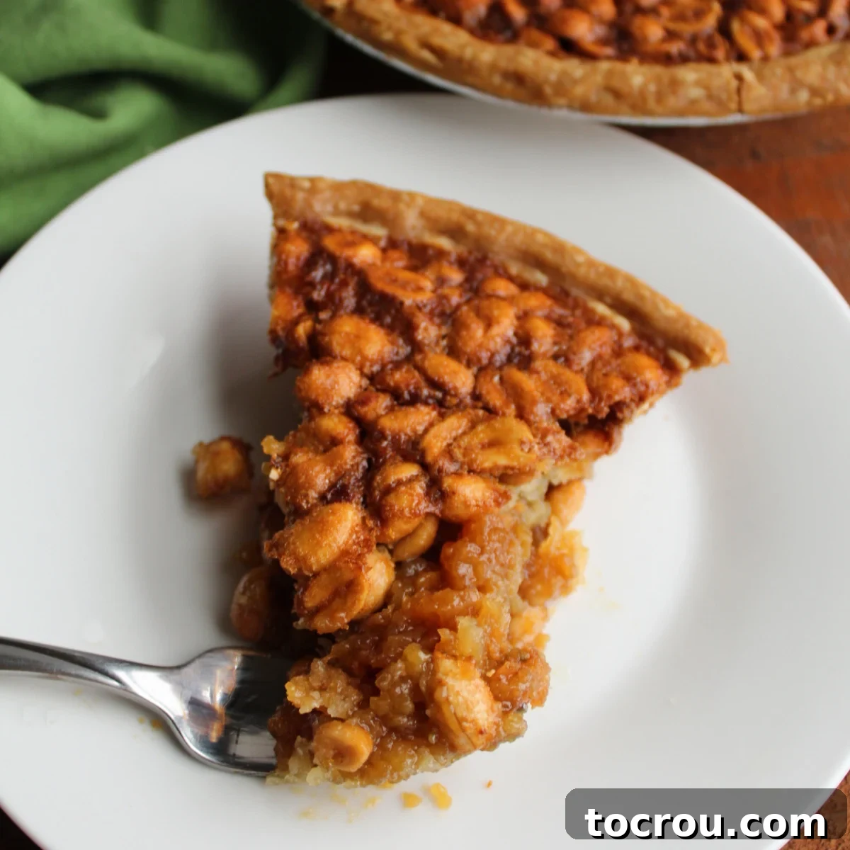 Close up of a slice of peanut pie with crunchy roasted peanuts in a gooey brown sugar filling, ready to be enjoyed.