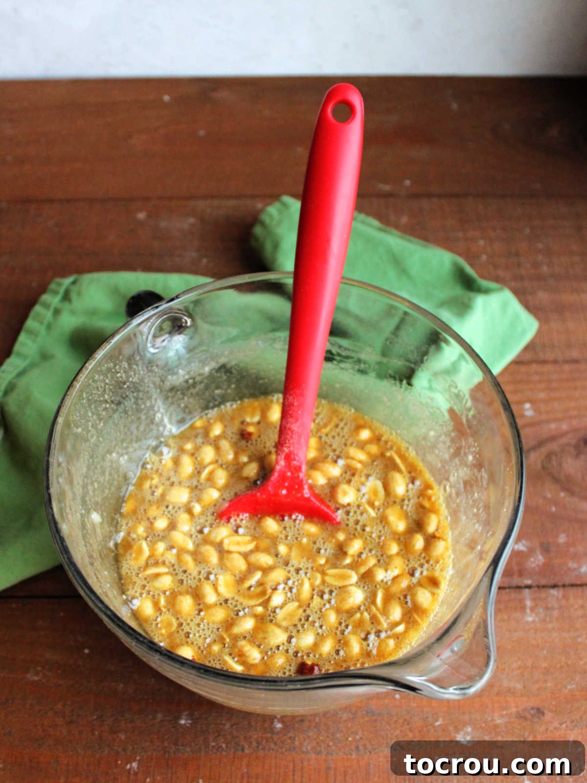 Mixing bowl with creamy peanut pie filling, featuring roasted peanuts suspended in a golden mixture of brown sugar, eggs, and other ingredients, ready for the pie shell.